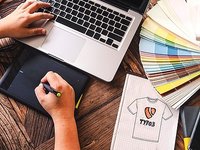Hands designing and typing next to scribble of TYPO3 t-shirt
