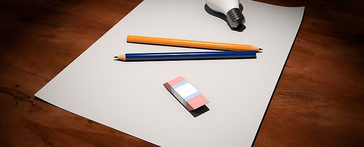 Pencils, rubber and a lightbulb on white paper sheets